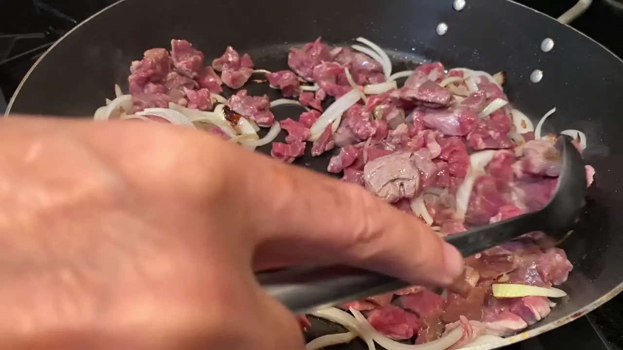 Unrecognizable hand cooking meat with onions