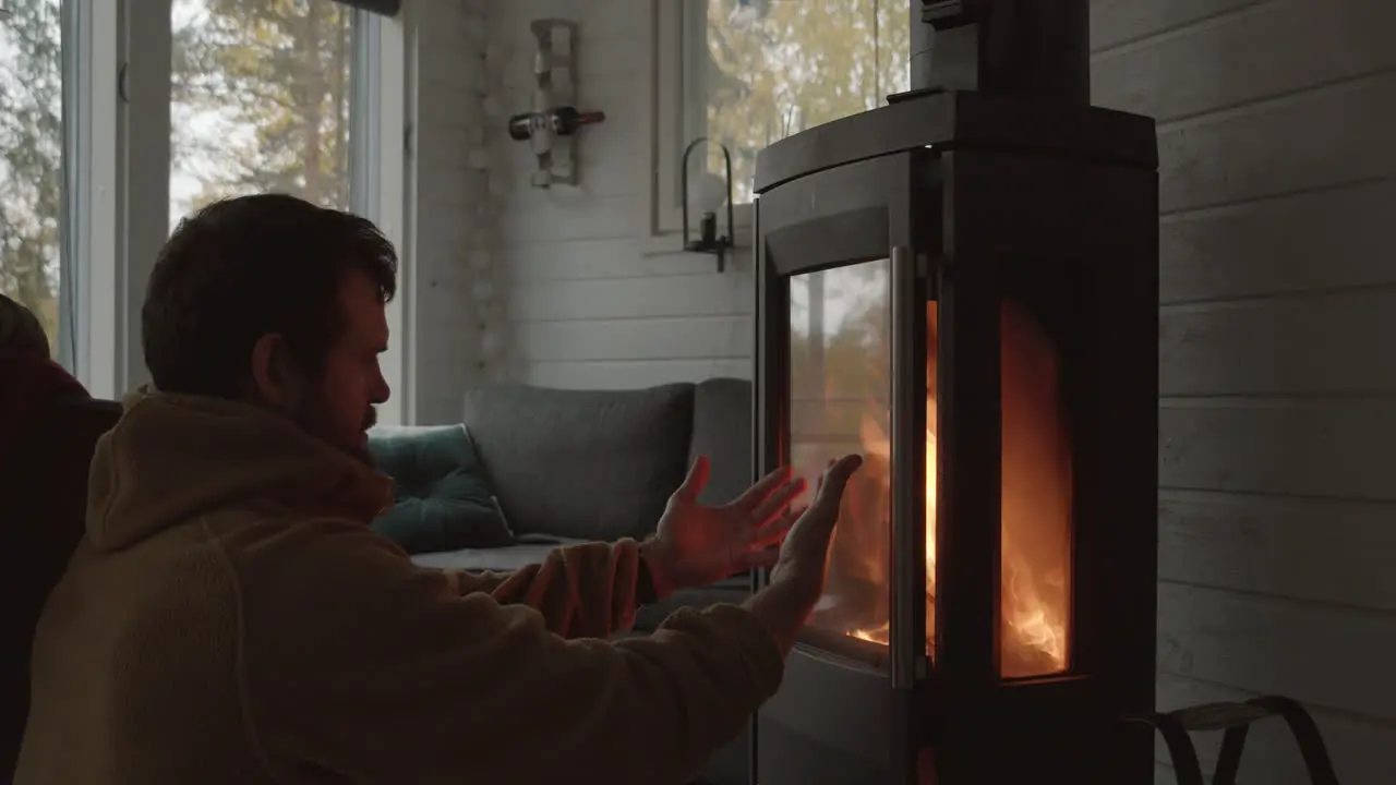 Man sits in front of indoor fireplace warming his cold hands Medium close