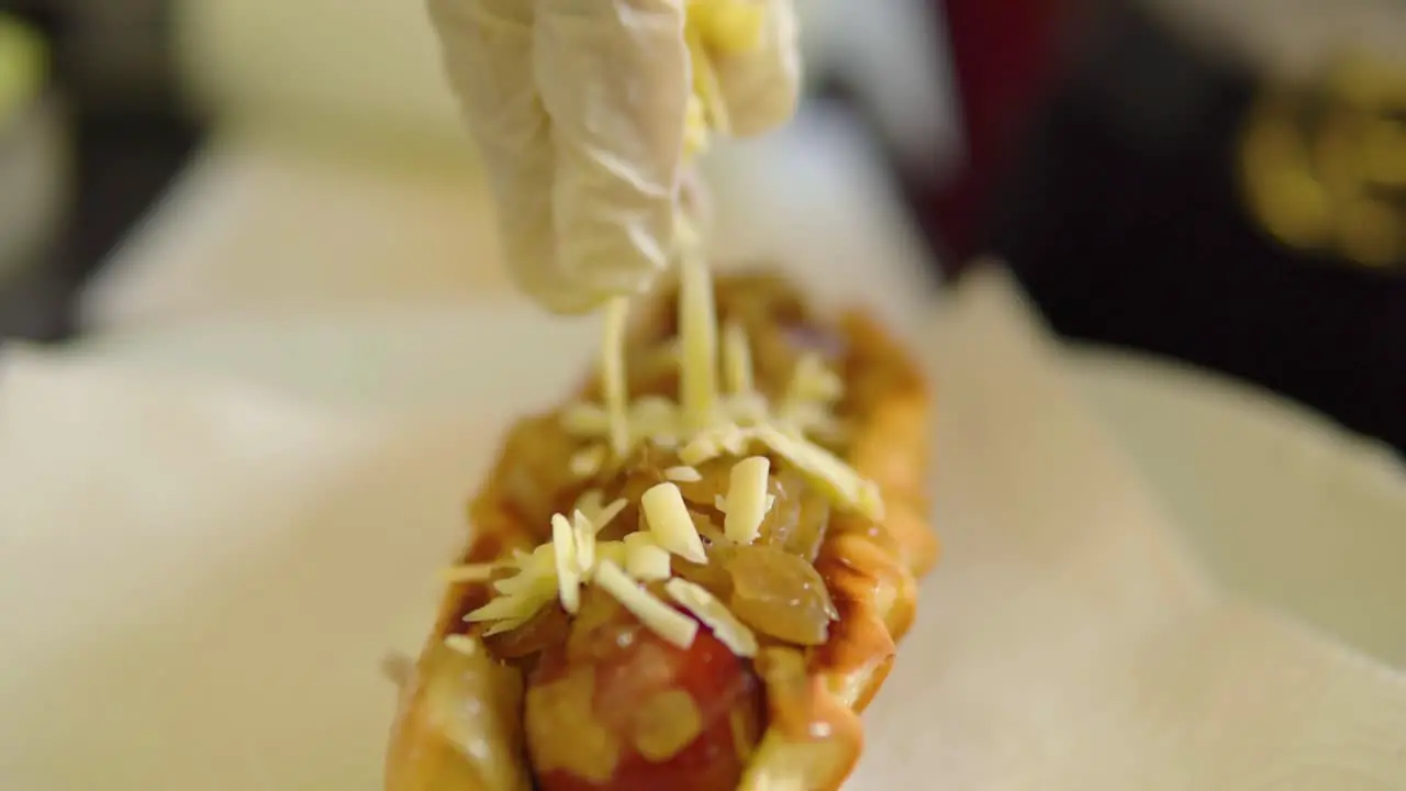 Putting grated cheese on top of freshly grilled hotdog