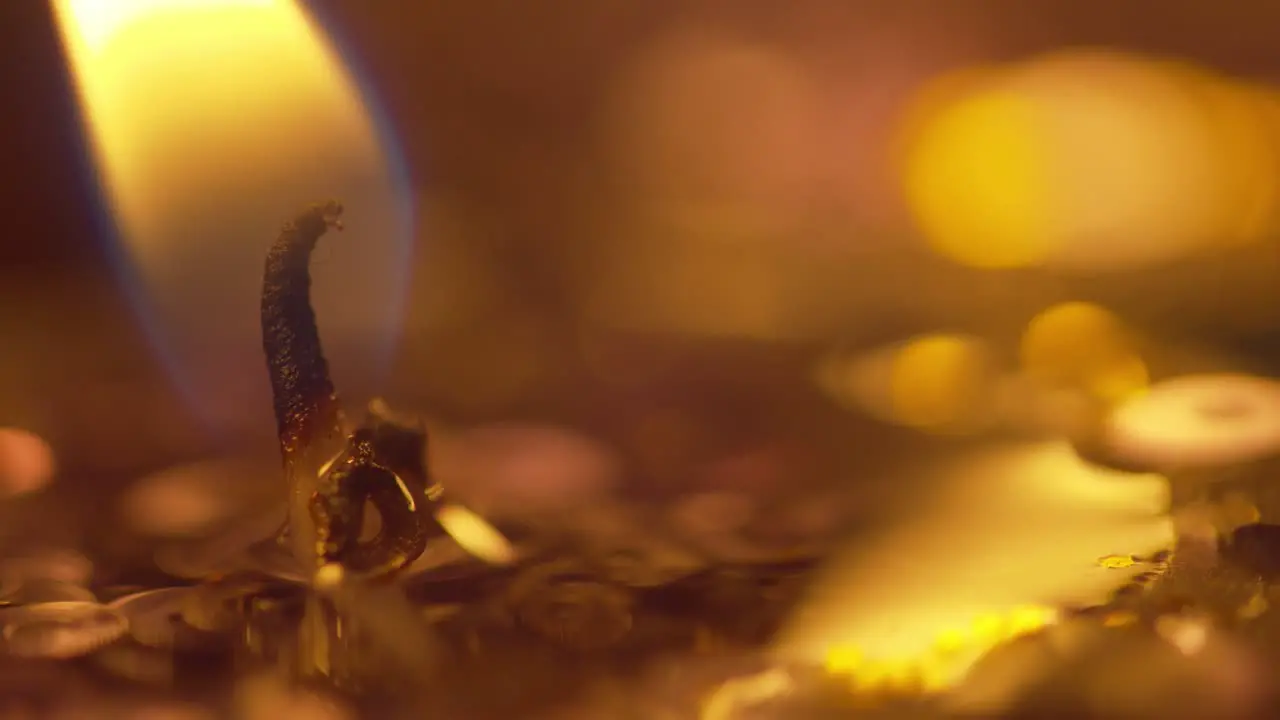 Macro look at the golden flame from a candle and wick with sparkle and bokeh from the candles in the background static