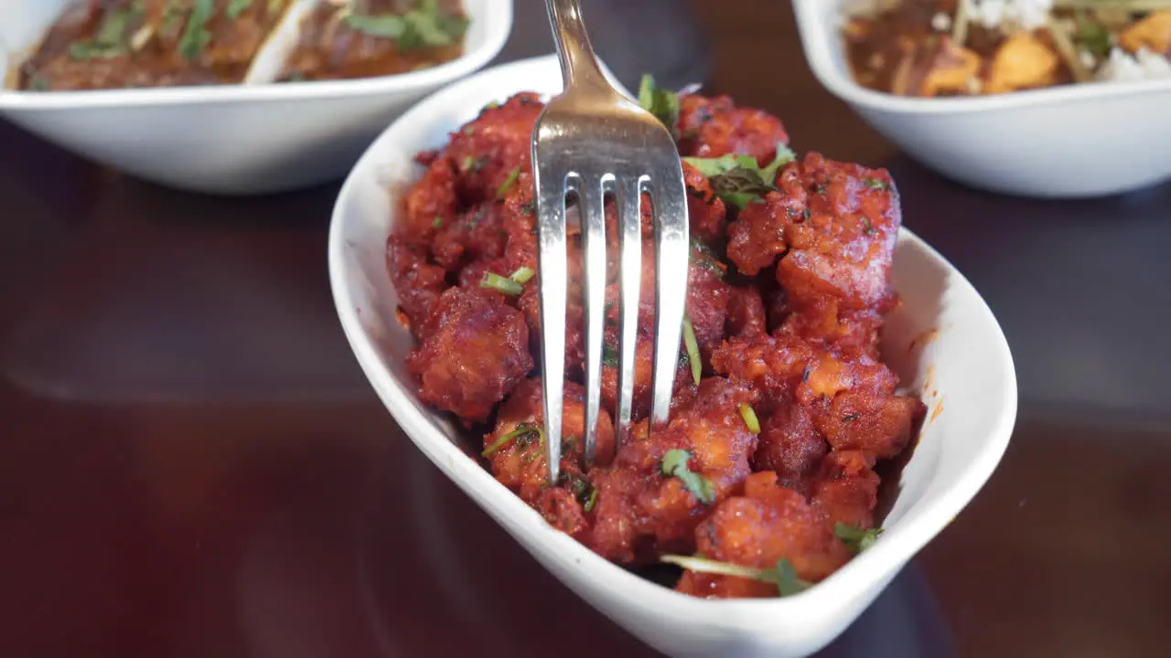 Fork picks up gobi manchurian a bite of fried cauliflower in spices slider close up 4K