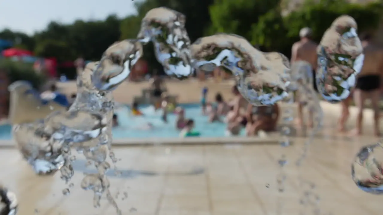 Water fountain in slow motion in a camping people chilling in a pool background