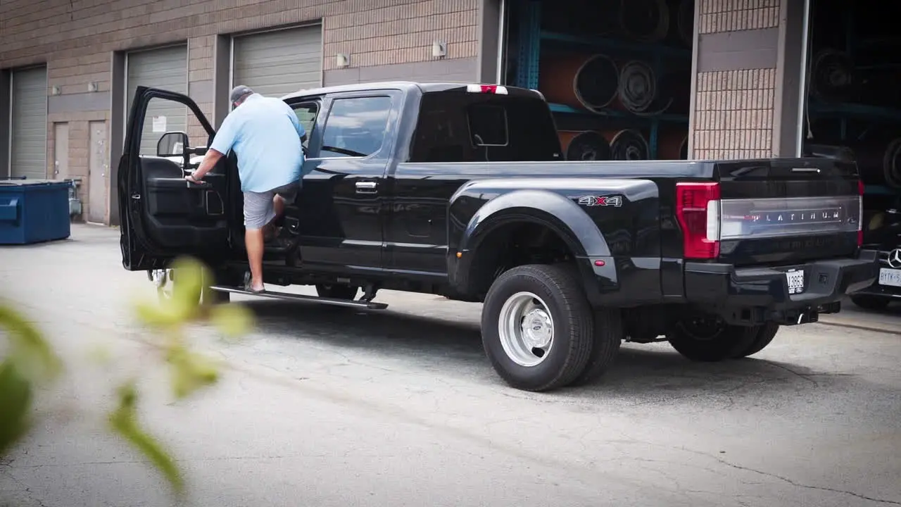 Man entering his pickup truck and driving away behind a warehouse