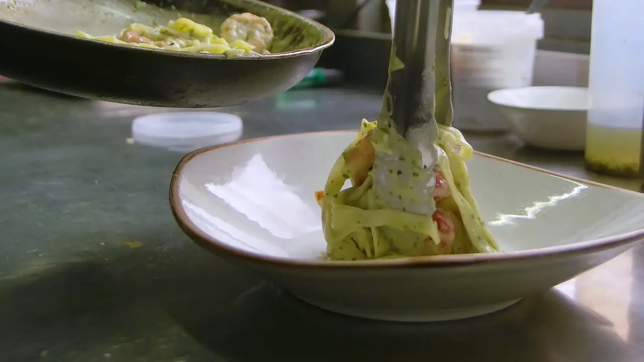 Chef places seafood white sauce pasta on plate with tongs