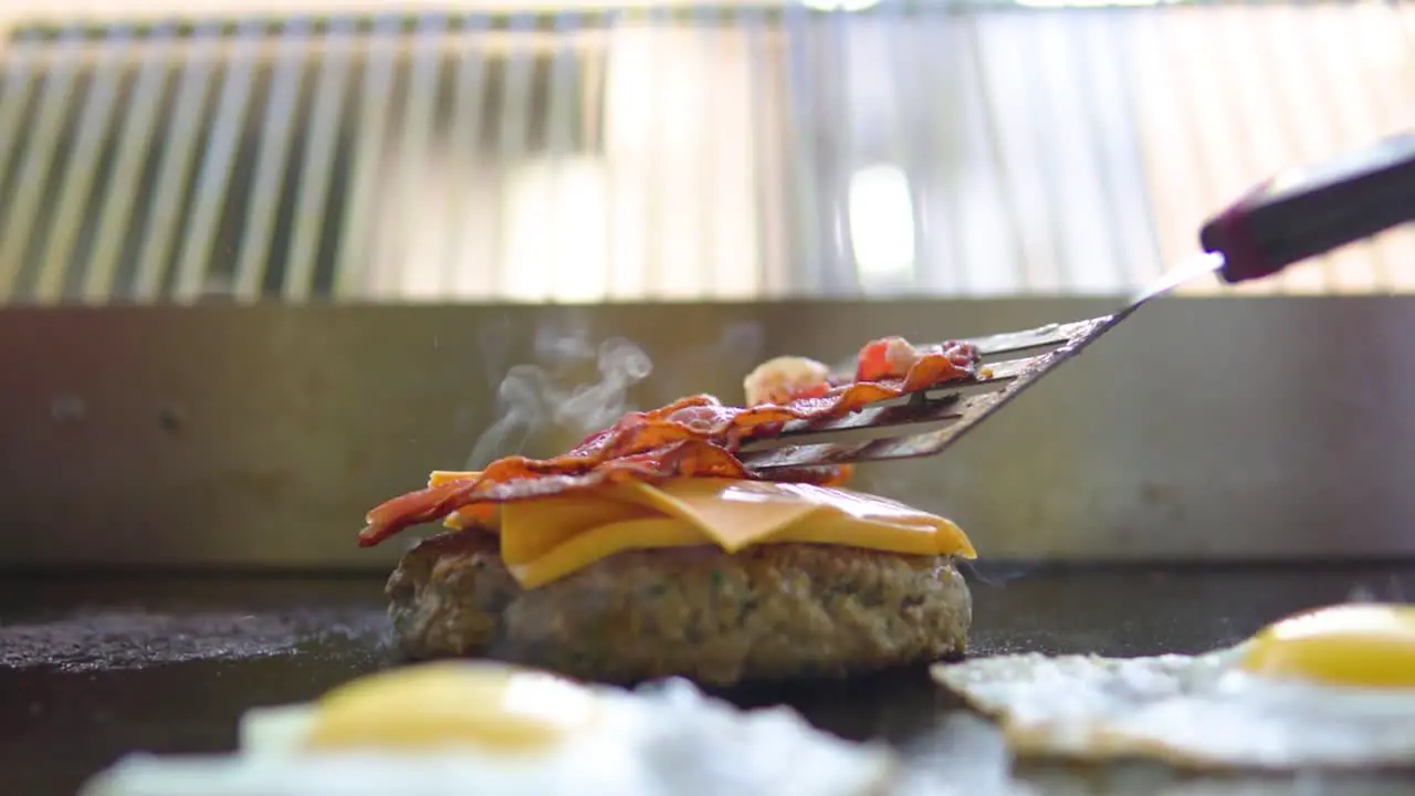 Placing bacon on a cheeseburger in fast food restaurant close up slow motion