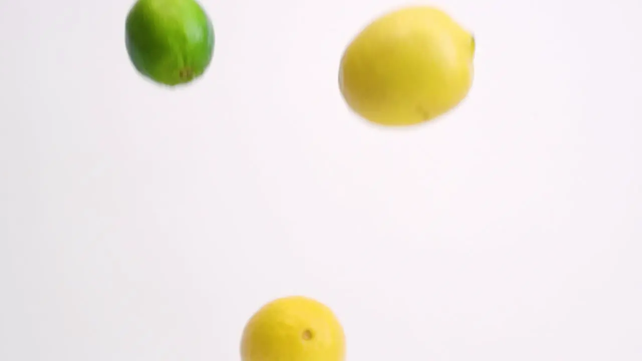 Whole lemons and limes falling in slow motion on white backdrop and bouncing around