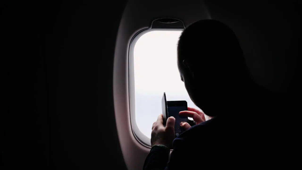 A Silhouette Of A Man Taking Pictures Of The View From The Plane Window