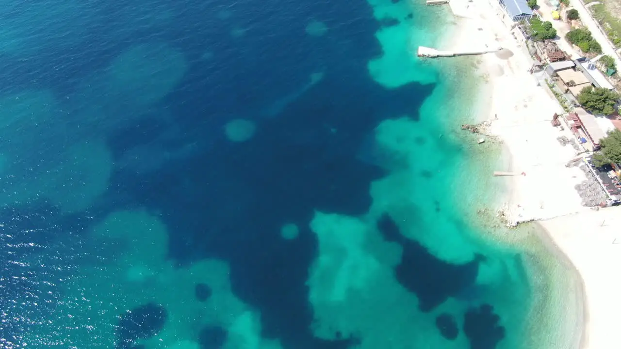 Drone view in Albania flying over white sand beaches blue crystal clear water with different hues on a sunny day in Ksamil