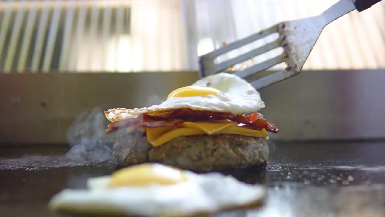 Placing freshly cooked bacon and egg on a cheeseburger which is still being grilled in fast food restaurant