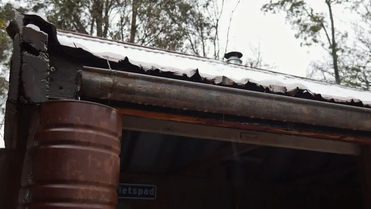 Water flows from a gutter into a rustic downpipe on an old building during rain