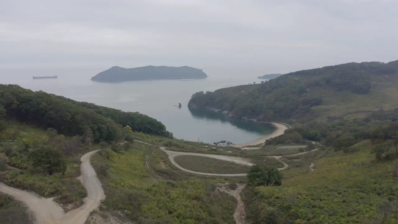 View of a bay surrounded with green forest and an island in far distance on a cloudy overcast day