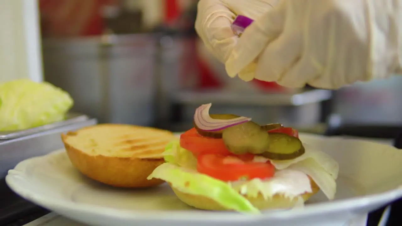 Placing onions on a bun with vegetables ready for burger in fast food slowmotion