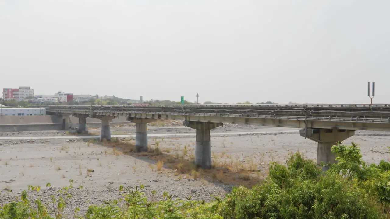 A long road bridge passing across a large dry river under an overcast summer sky in southern Taiwan wide shot