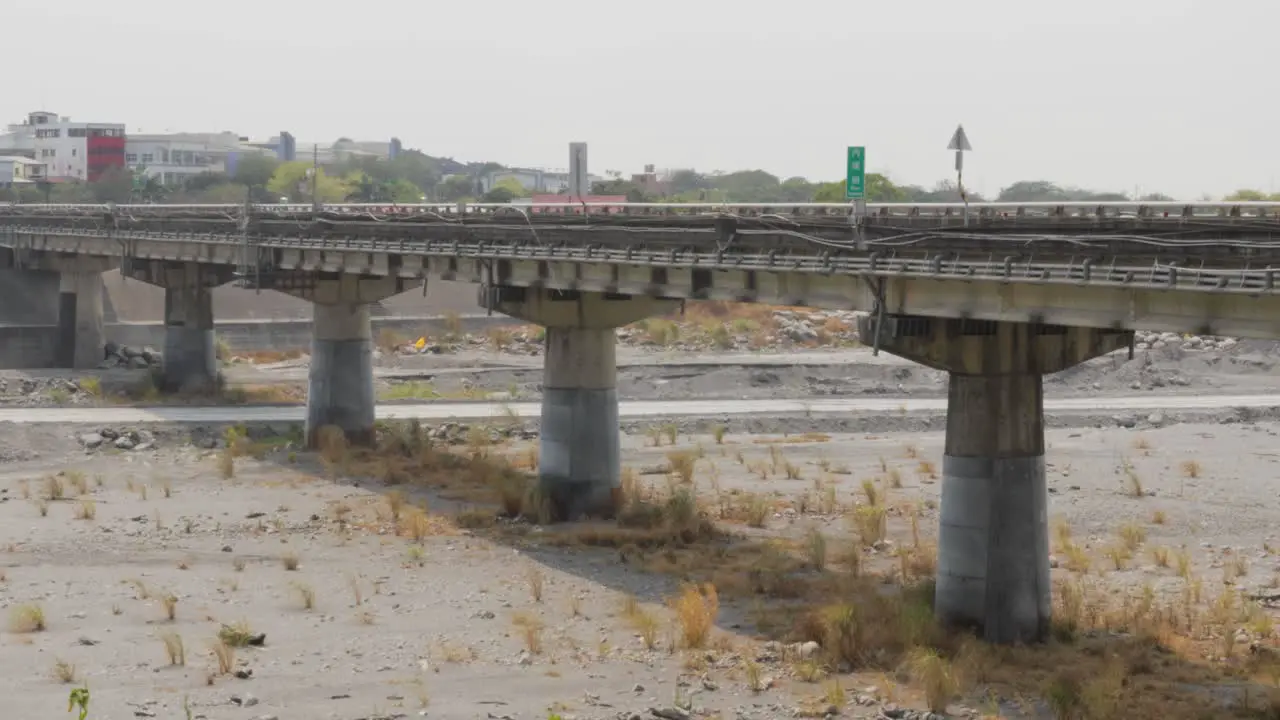 A long road bridge passing across a large dry river under an overcast summer sky in southern Taiwan medium wide shot