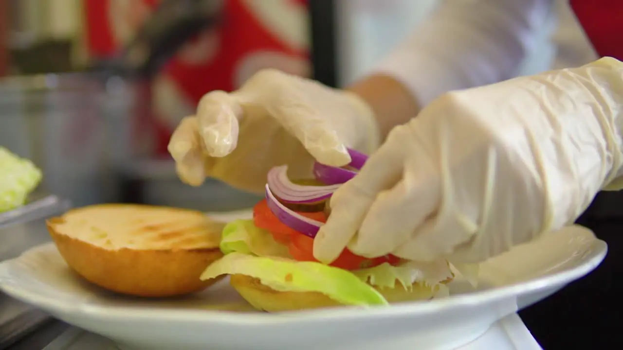 Chief with gloves putting vegetable on a bun for hamburger