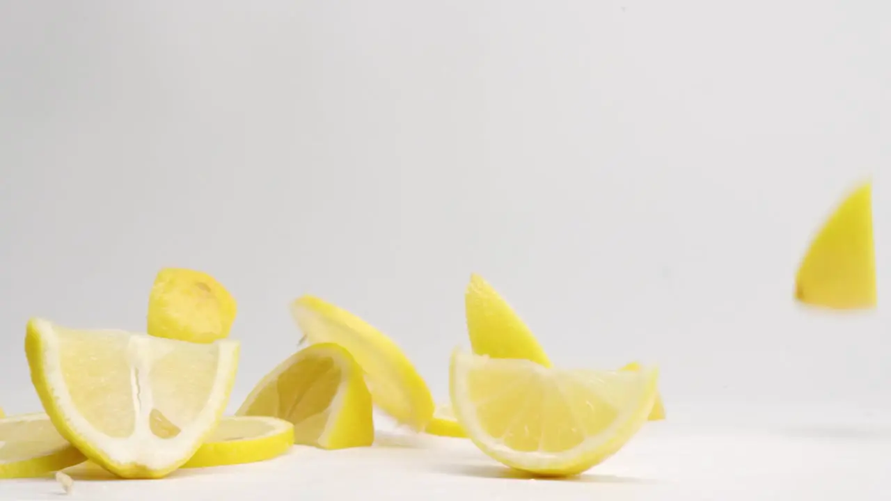 Slices and wedges of bright yellow lemons bouncing on white table top in slow motion