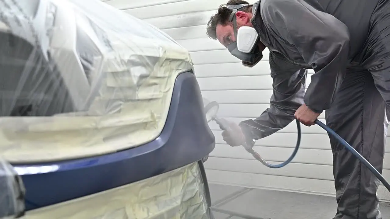 Painter with protective mask spray painting vehicle slow motion view