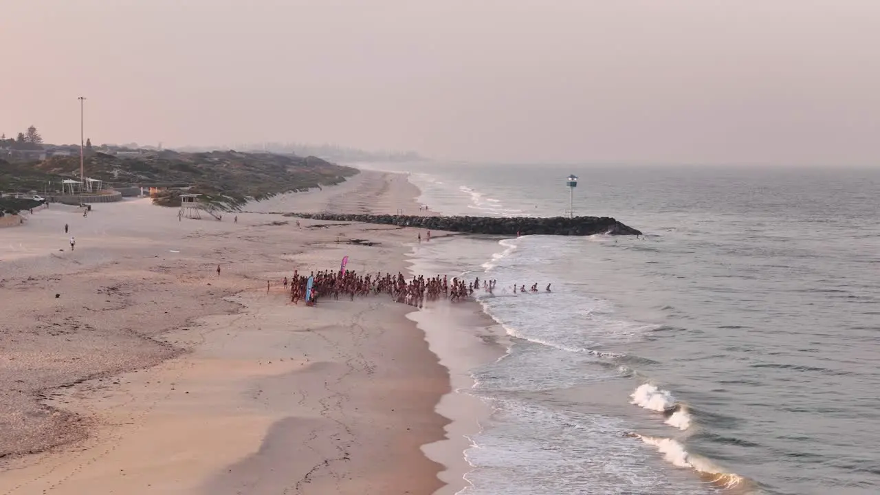 Group of swimmers running into the ocean at sunrise for a cold dip