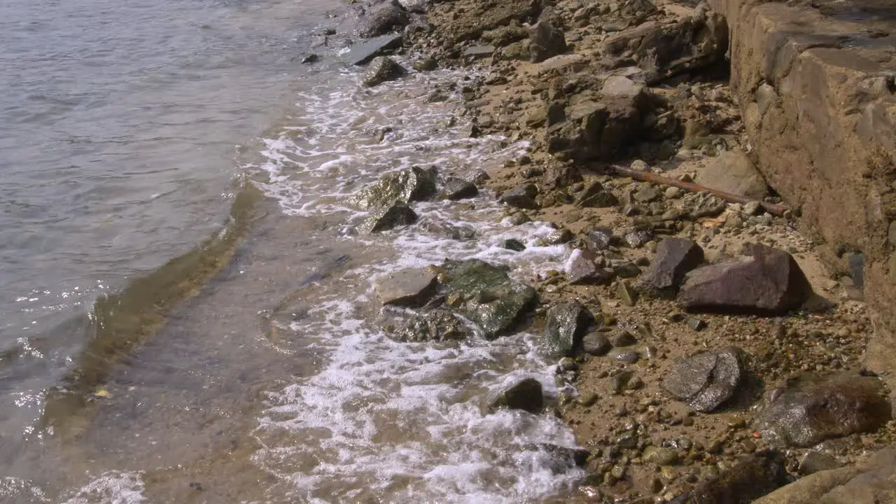 Wide shot of small waves rippling against a rocky beach on a sunny day