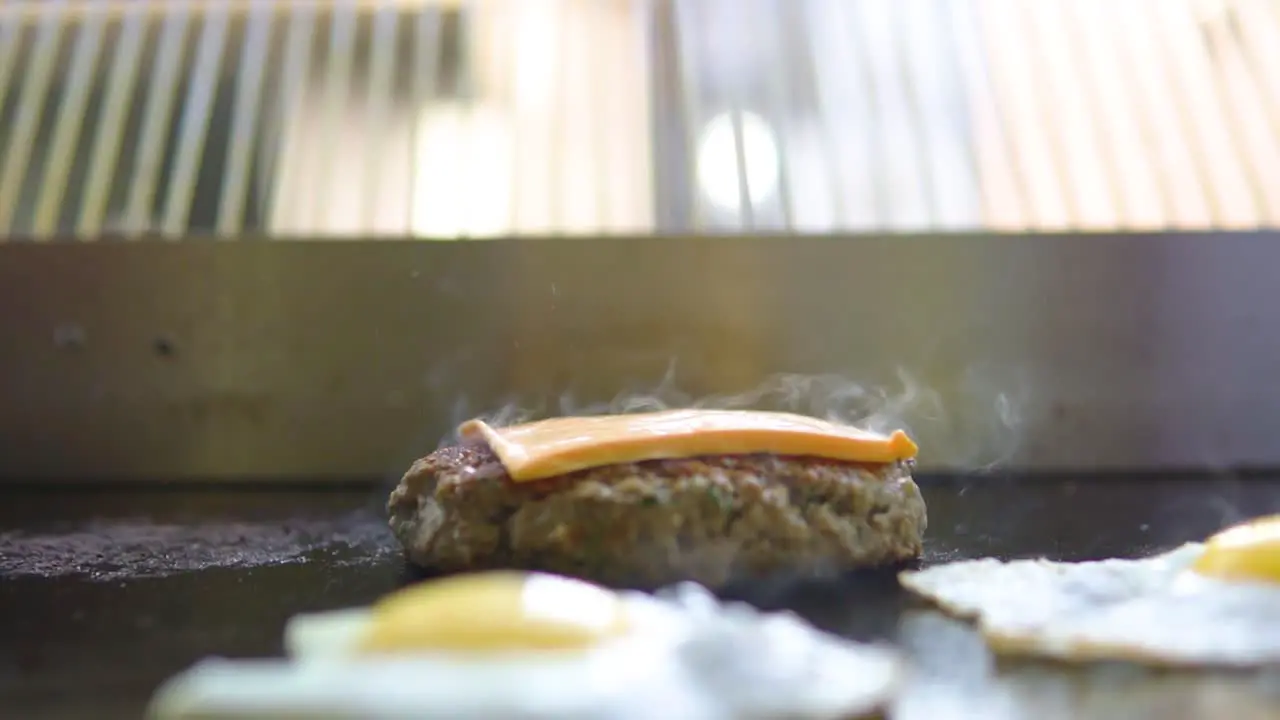 Placing cheese on a smoking grilled burger in a fast food window shop