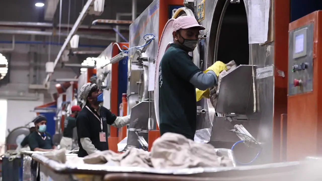 Male Workers Emptying Out Large Industrial Tumble Dryers In Factory In Pakistan