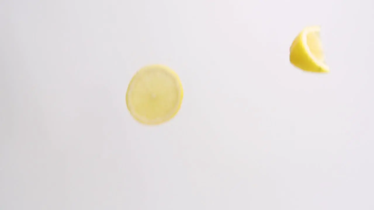 Slices and wedges of bright yellow lemons raining on white backdrop in slow motion