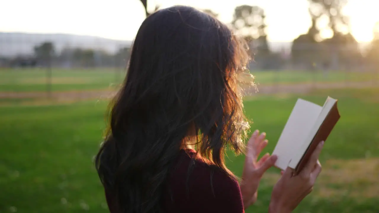 A young woman reading a story book outdoors in the park at sunset with light shining bright