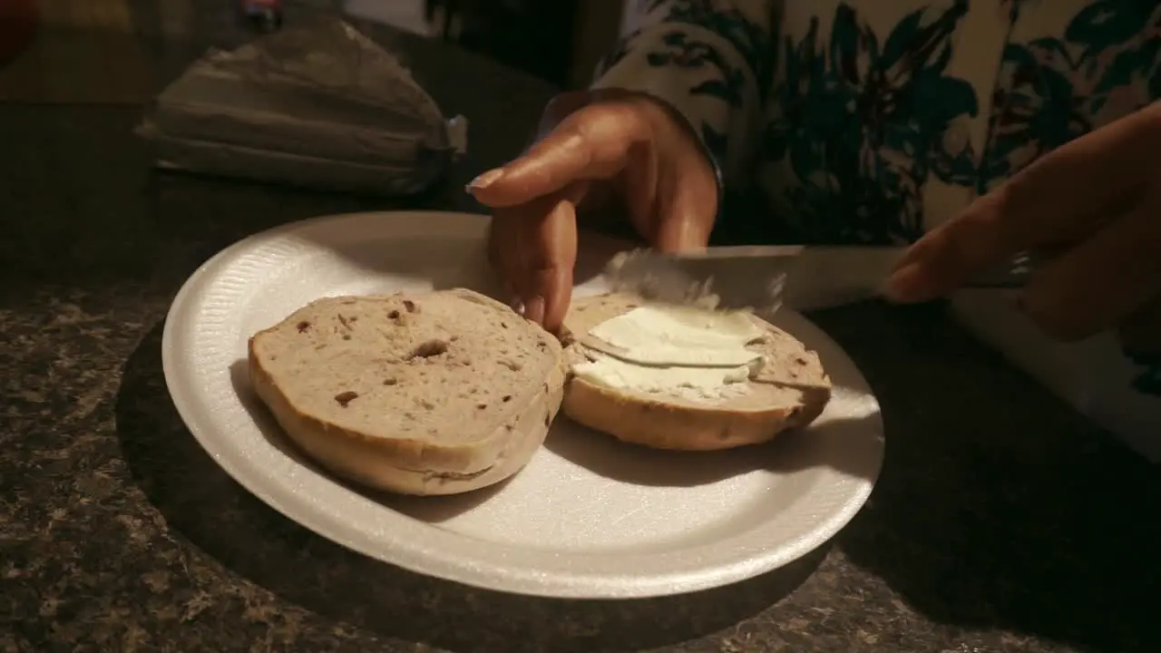 Black young female smearing cream cheese on a bagel for breakfast