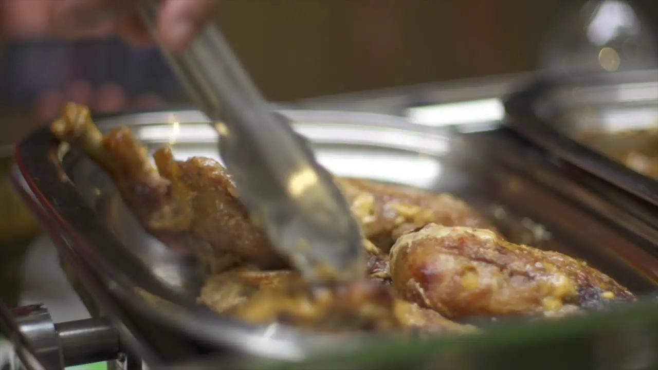 Fired chicken thighs arranged into stainless steel pan using tongs filmed as close up