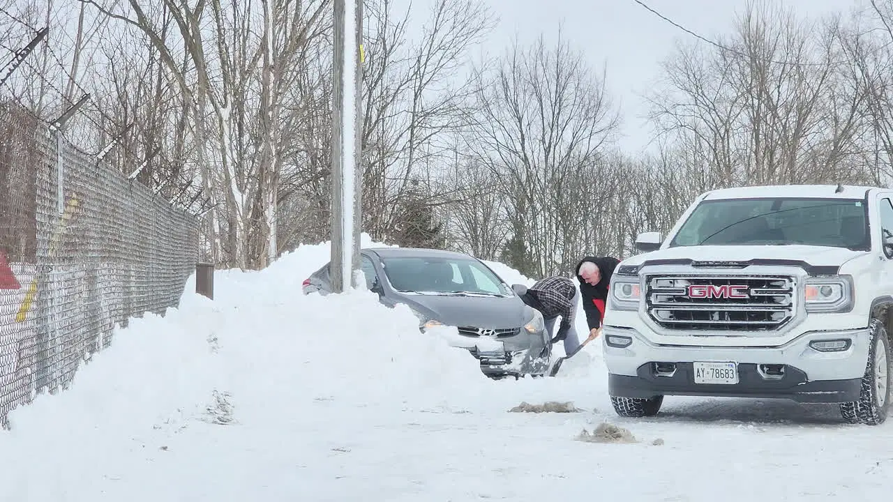 People in the street clearing snow next to a car After Winter Snow blizzards Canada