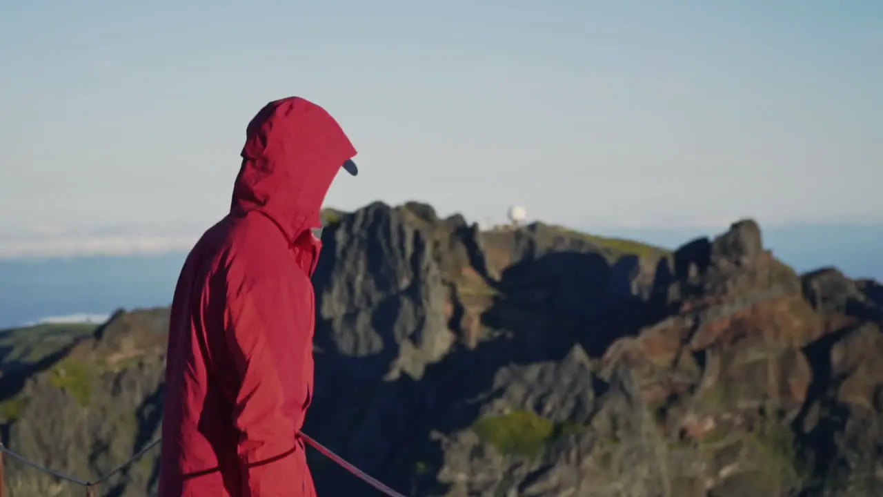 Person in red jacket looking out over mountains with observatory in distance