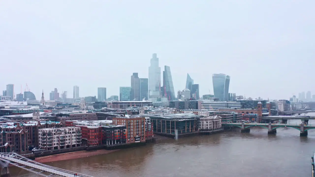 Rising London aerial drone shot of snow falling on city of London skyscrapers from river thames