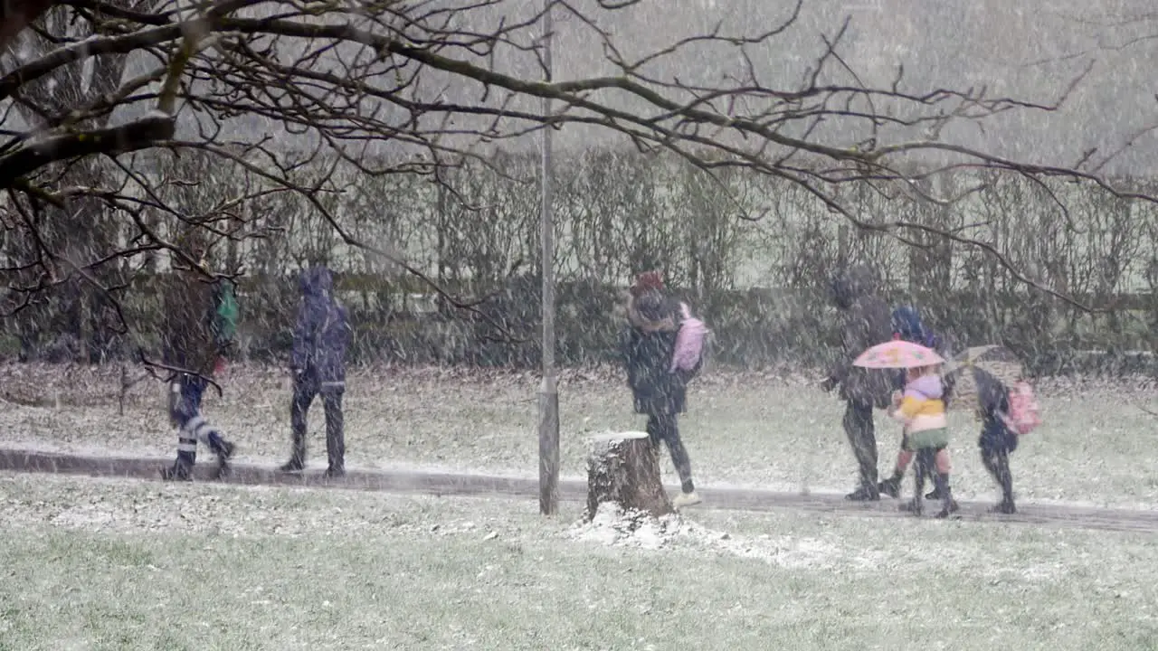 People walking children to school in blizzard snow cold weather in windy UK winter storm conditions