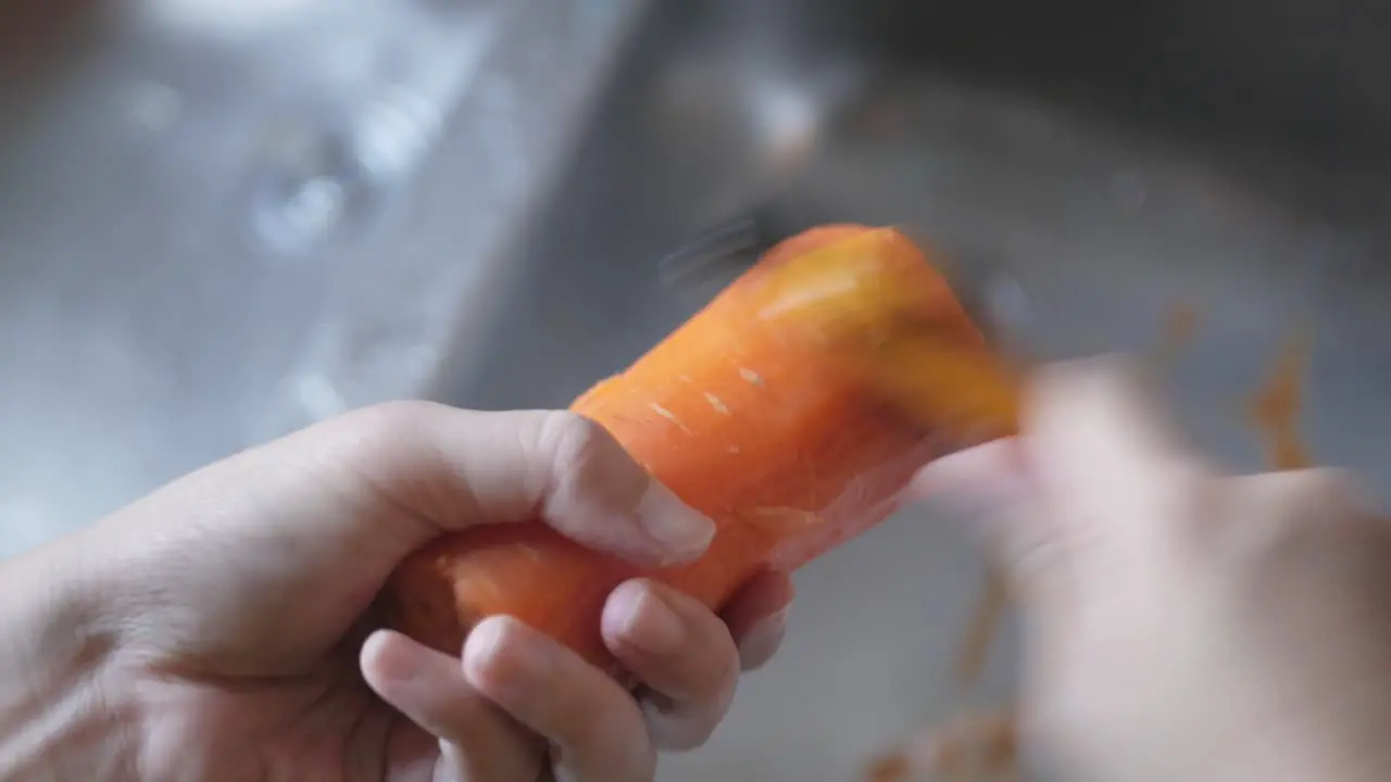 hand using peeler to peel fresh carrot skin preparing for cooking