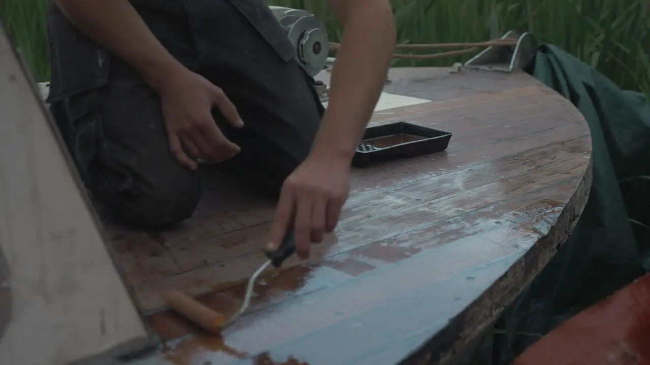 Varnishing deck bow of wooden boat with roller