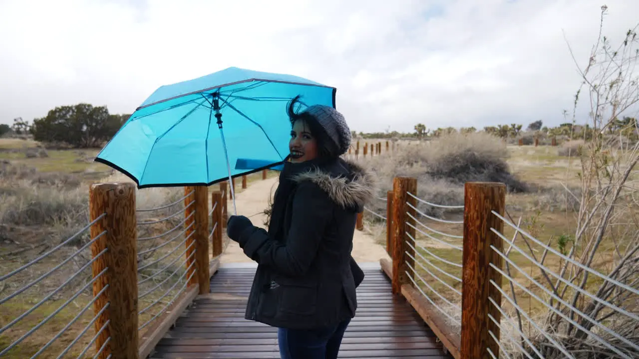 A pretty woman walking across a bridge with a blue umbrella during a rain storm in bad weather SLOW MOTION