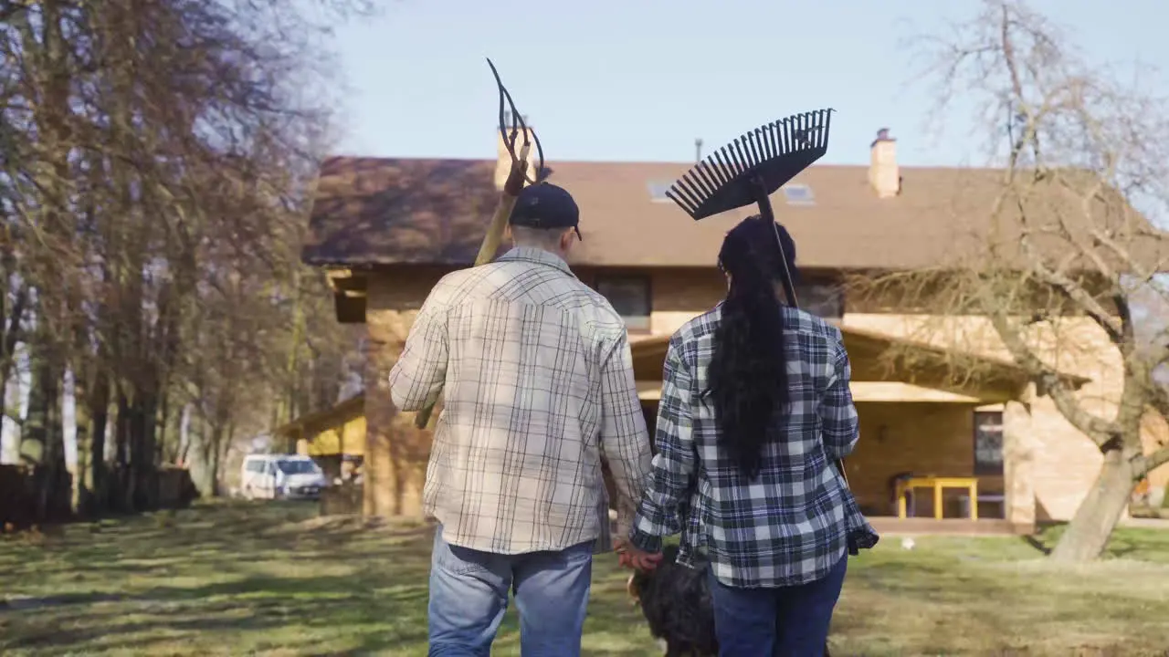 Rear view of caucasian holding hands and carrying rakes while walking throught the countryside