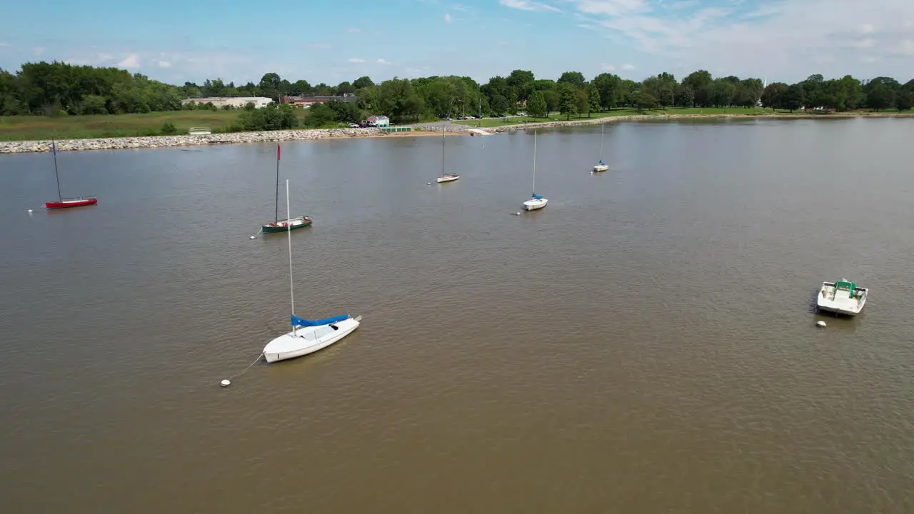 Drone low flight over moored sailboats calm river sunny day left to right gentle twist around boats