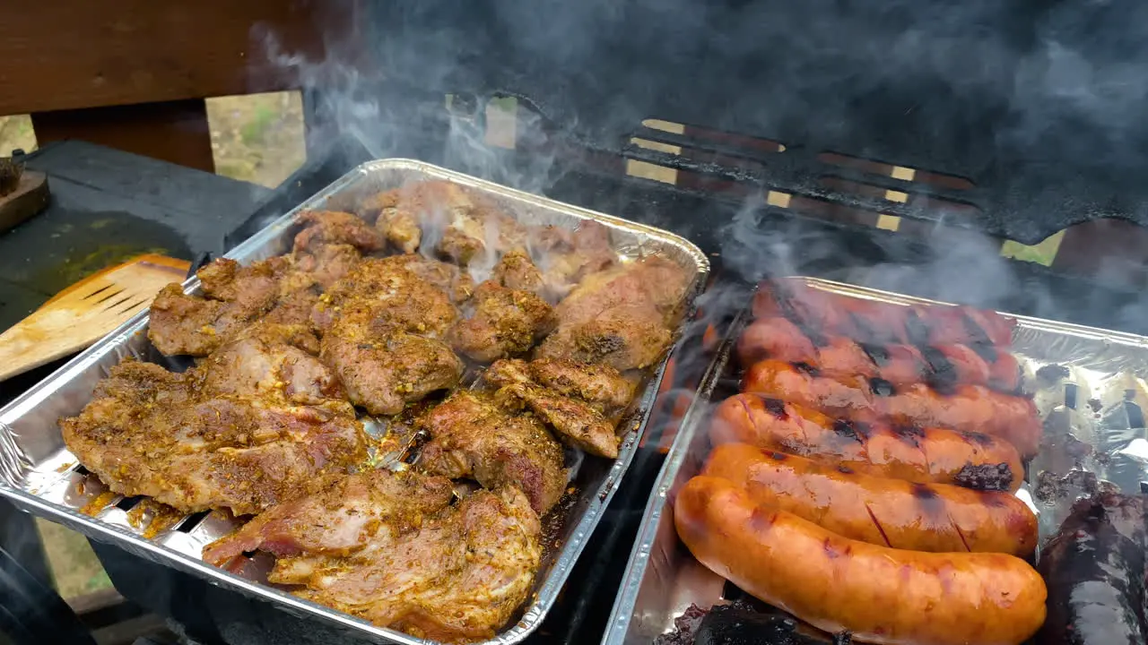 Marinated chicken breast and german sausages grilled on metal trays outside the house during the daytime