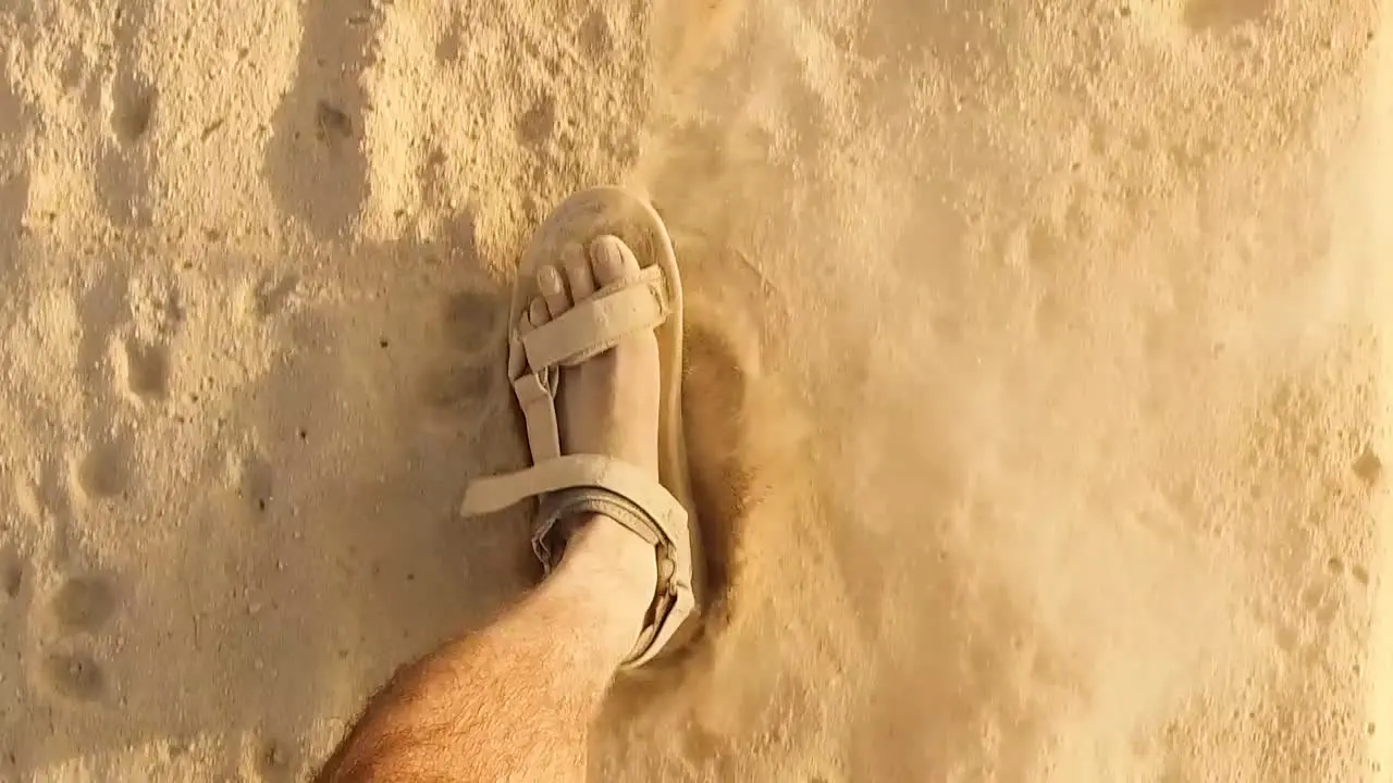 Closeup Caucasian man's with dusty feet walking slow motion with Sandals On Sandy desert or Beach Footprints Kicking some particles sparkling dust sand wearing sandals in sunny day