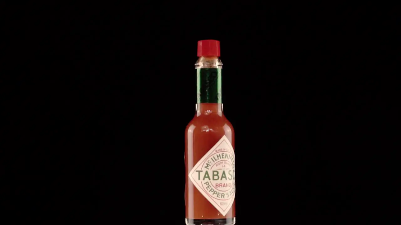 Static Slow Motion Shot Of A Tabasco Bottle Turning On Itself With Red Chili Peppers Poping Up Behind it Shoot in a Studio with Black Background