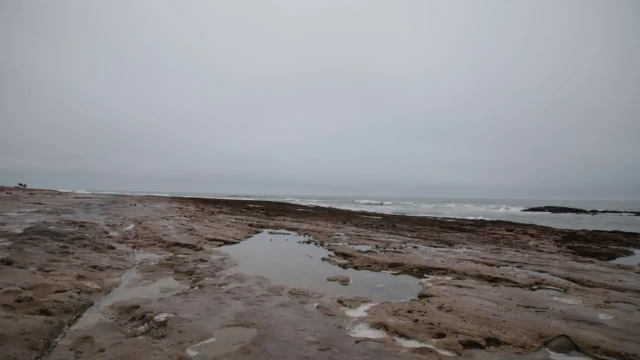 A puddle on a rocky beach with the ocean in the background on a cloudy day