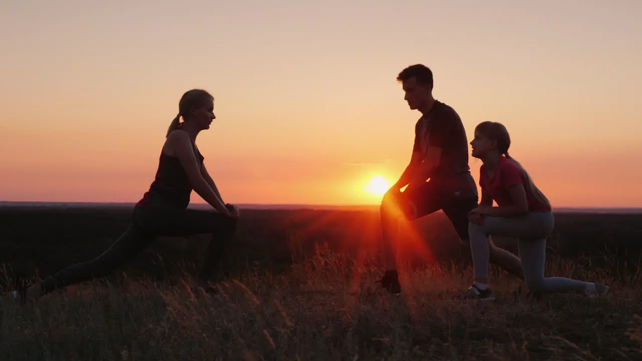 Family With A Child Doing Exercises Together In A Picturesque Place At Sunset