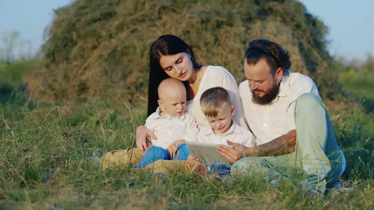 Young Parents Are Resting With Their Children During The Weekend In Nature Playing On The Tablet