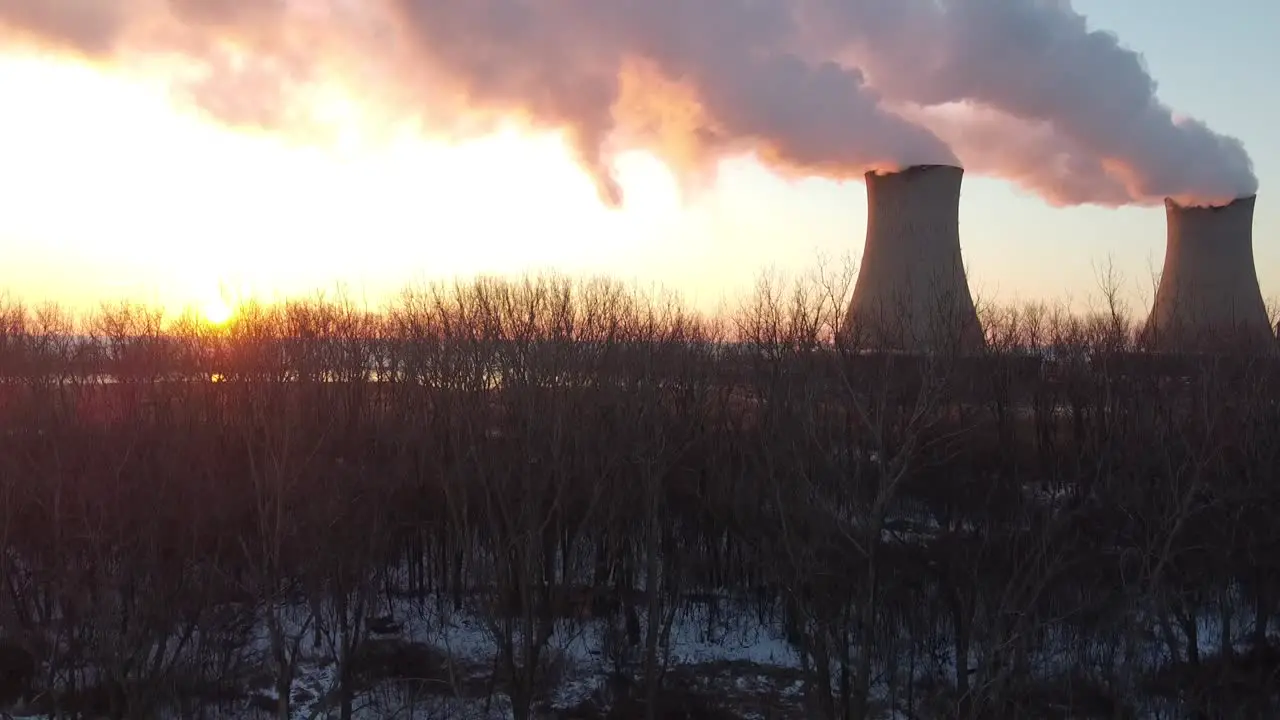 Dolly up aerial drone shot of Nuclear Power Plant Cooling Towers at Sunrise Sunset with Steam and Smoke bright sun winter