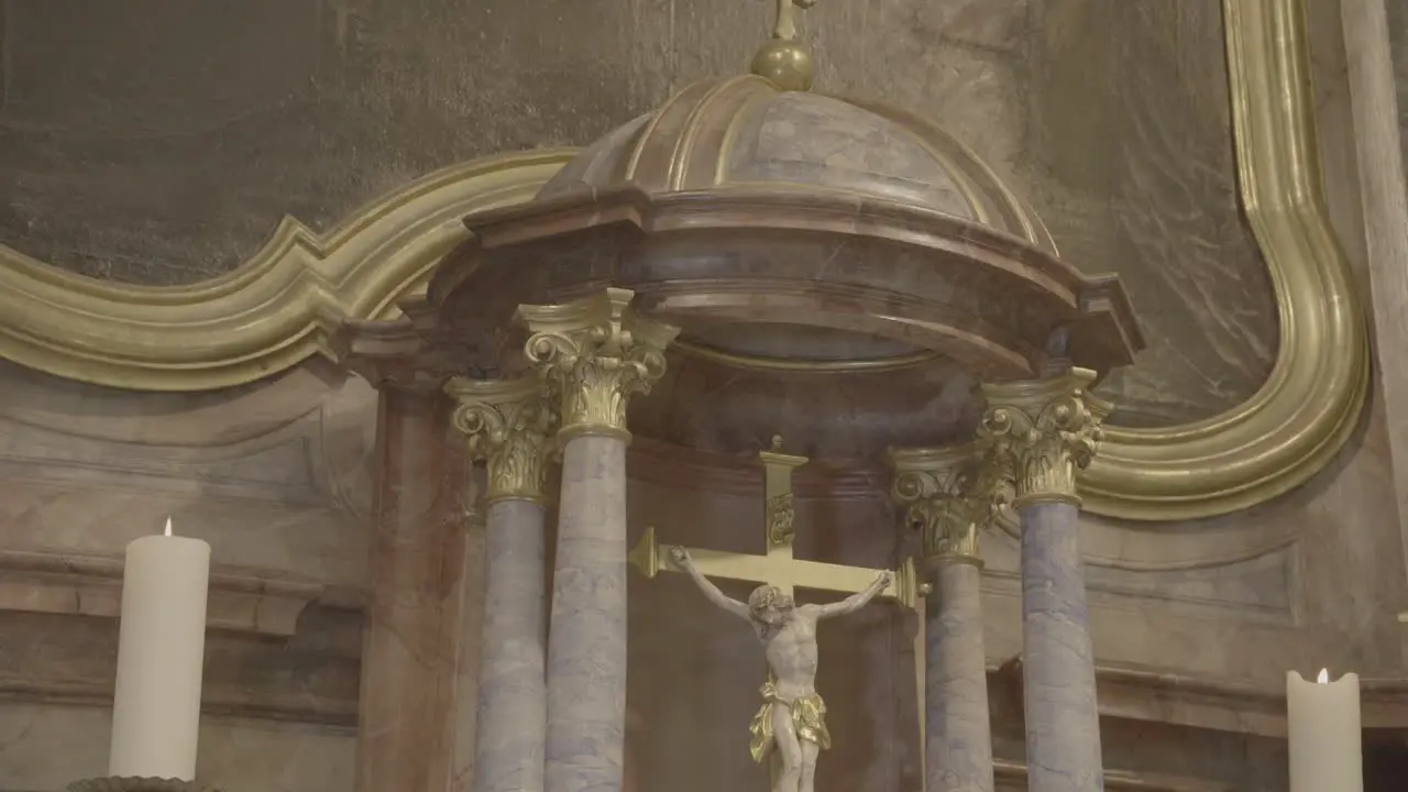 Camera pans to a crucifix in a baroque altar between two candles