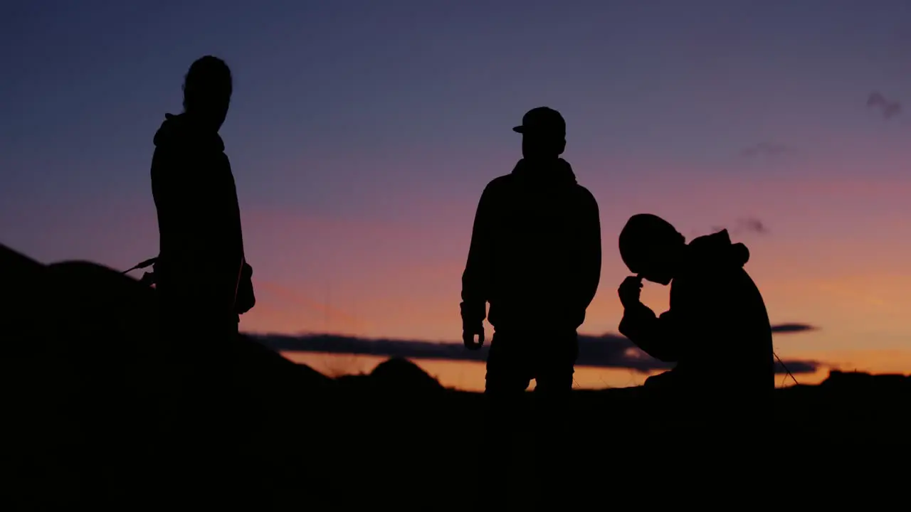 Three young motocross riders having a chat smoking cigarettes and enjoying the view of the epic shilouetted mountainscape