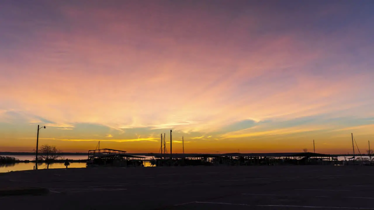 Person walks to boat house at early morning sun rises and shines rays between ship masts