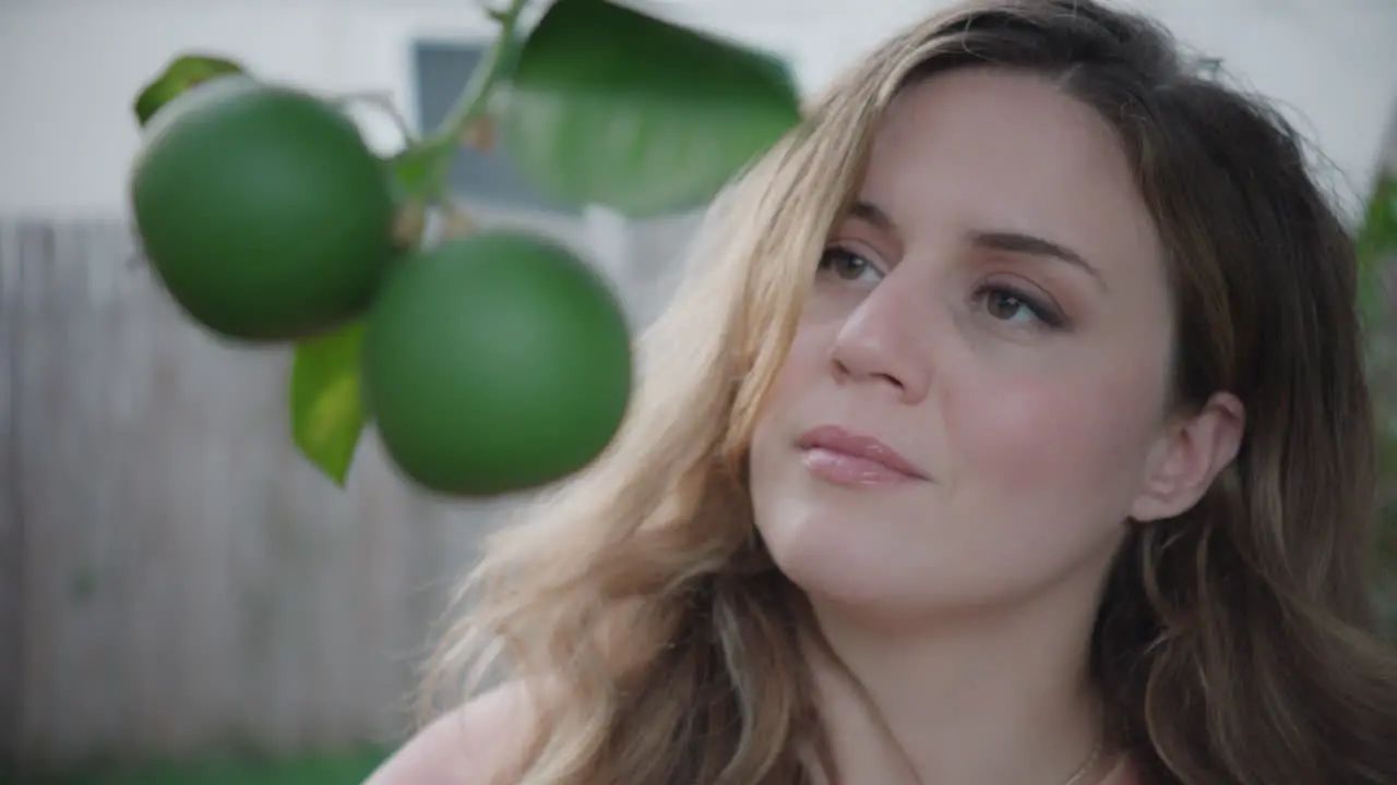 Brown Eyed Woman Admiring Citrus Plant Growing on Tree in Backyard Daytime Shot Outside