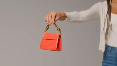 Close Up Of Female Social Media Influencer Producing User Generated Content Holding Out Orange Fashion Handbag